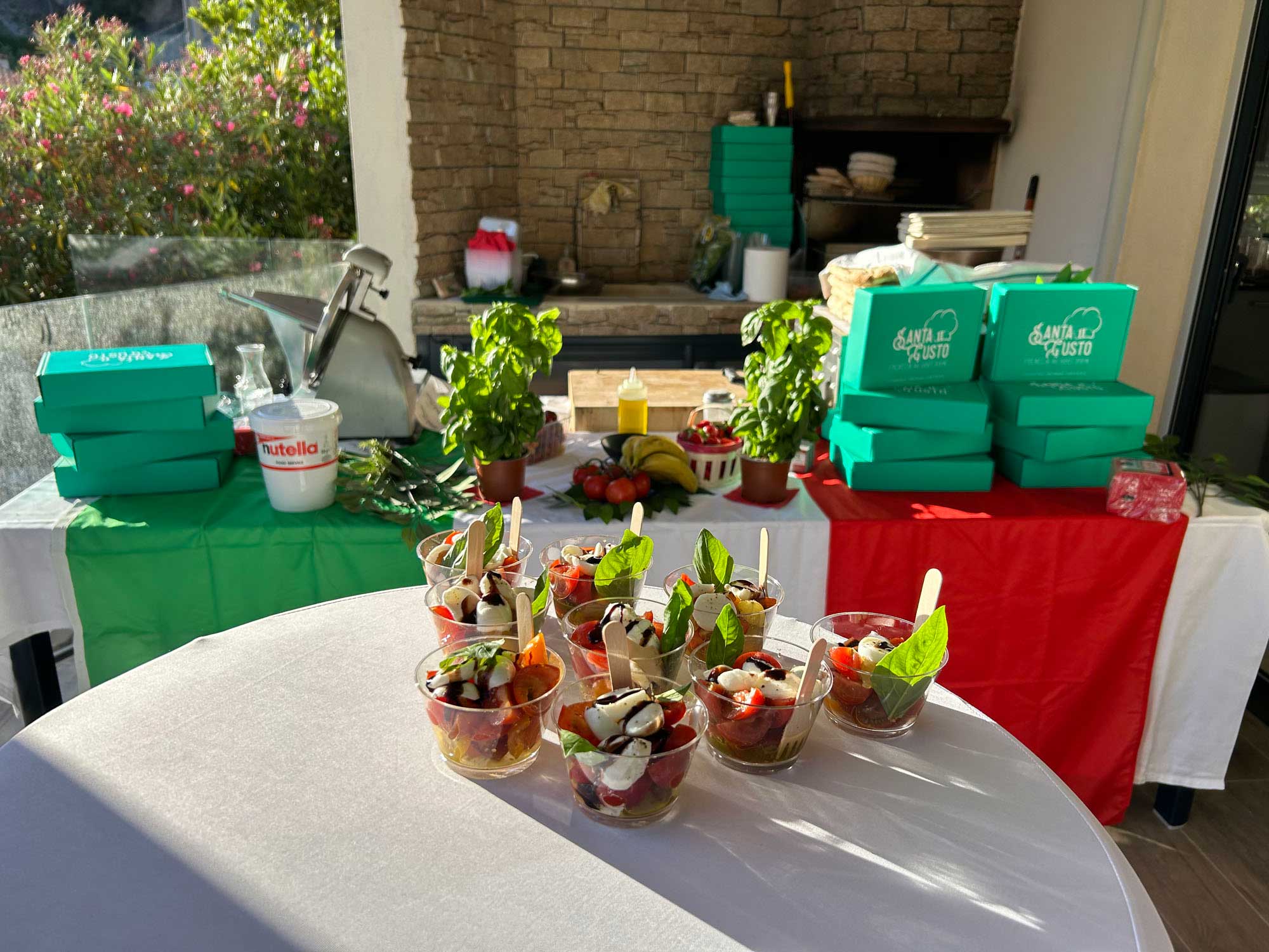 Photo d'une prestation traiteur avec une table composée de boites Santa Gusto et de verrines tomates mozzarella.
